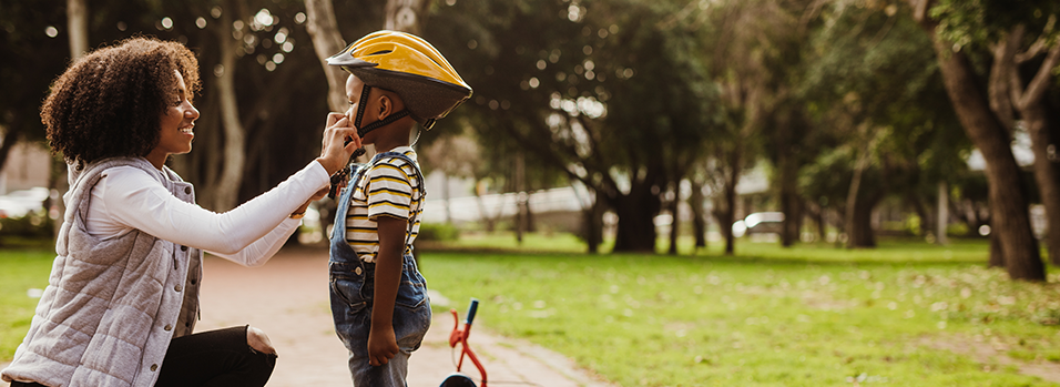 Mom helps her son put on a helmet so he can ride his bike safely