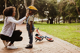 Mom helps her son put on a helmet so he can ride his bike safely